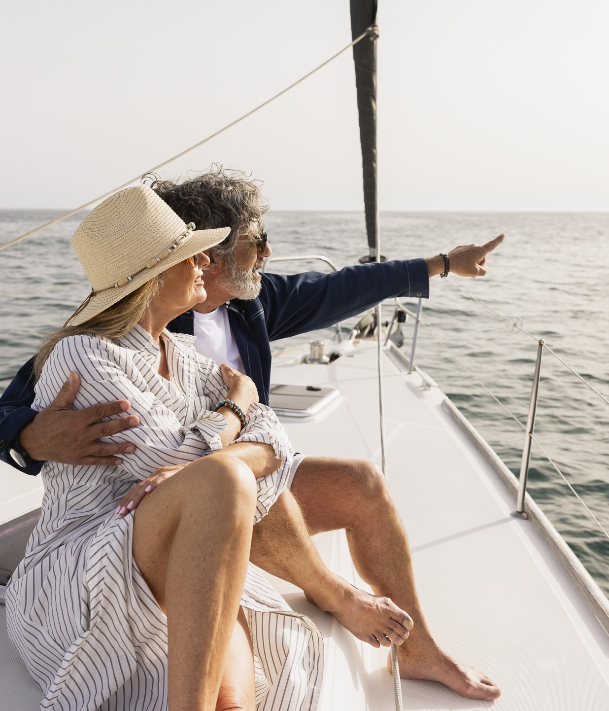 A retired couple relaxing on a sailboat, pointing out to sea